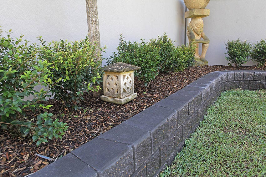 Decorative garden with stone lantern, plants, and a statue against a white wall.