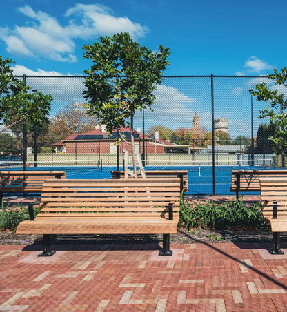 Wooden benches on a brick patio with a pool and fence in the background