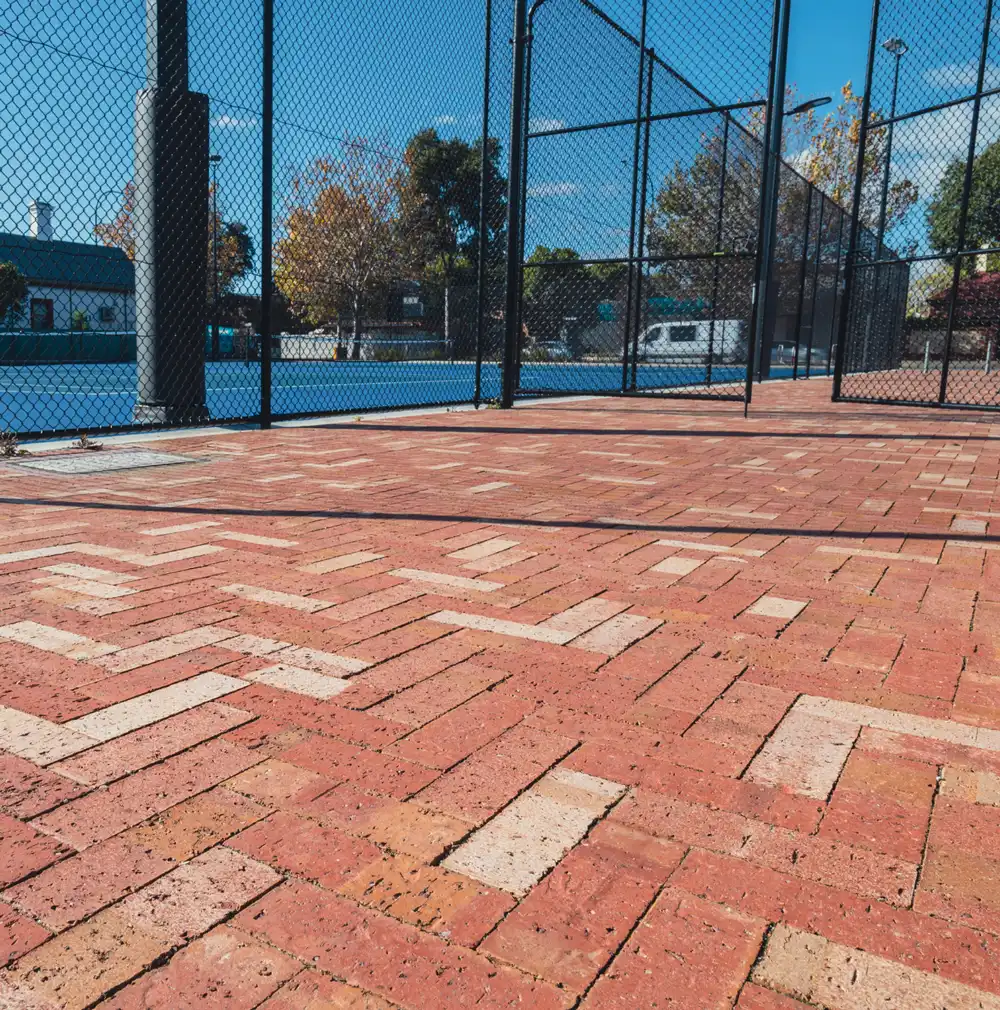 Brick patio area with a fenced tennis court in the background