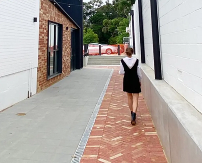 Person walking on a sidewalk next to a building with a red car in the background