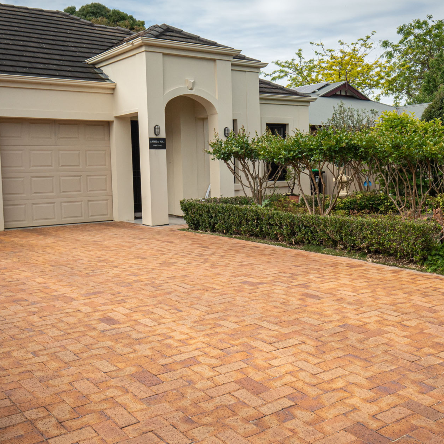 Brick driveway leading to a house with a garage and garden.