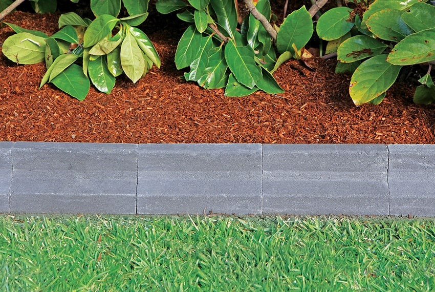 Gray stone border along a grassy area with mulched garden bed and green foliage.